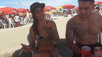 Une brune tatouée suce une bite sur la plage et avale du sperme